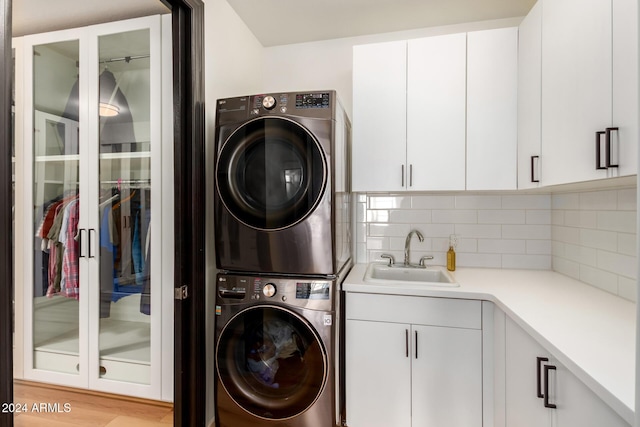 laundry room with sink, cabinets, stacked washer / drying machine, and light wood-type flooring