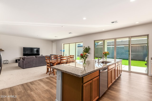 kitchen with dishwasher, light hardwood / wood-style flooring, light stone counters, sink, and a kitchen island with sink