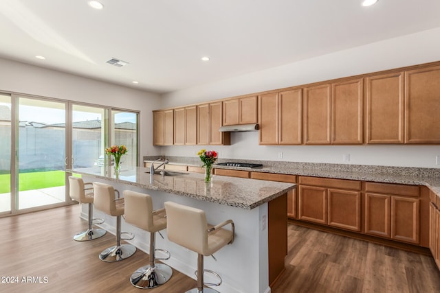 kitchen with stainless steel gas cooktop, dark hardwood / wood-style flooring, light stone counters, sink, and a center island with sink