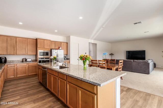 kitchen featuring appliances with stainless steel finishes, light stone counters, sink, dark wood-type flooring, and a center island with sink