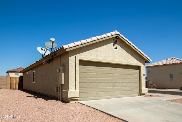 view of home's exterior featuring a tiled roof, stucco siding, driveway, and fence