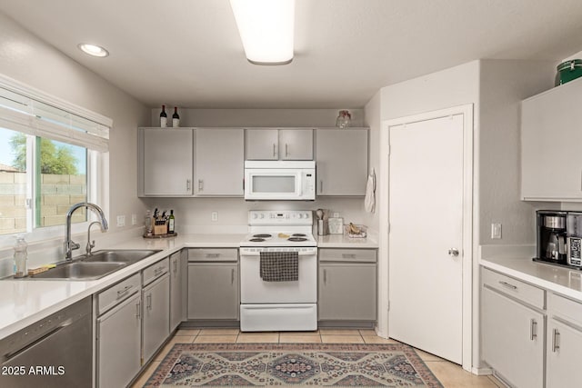 kitchen with light countertops, light tile patterned floors, gray cabinets, white appliances, and a sink