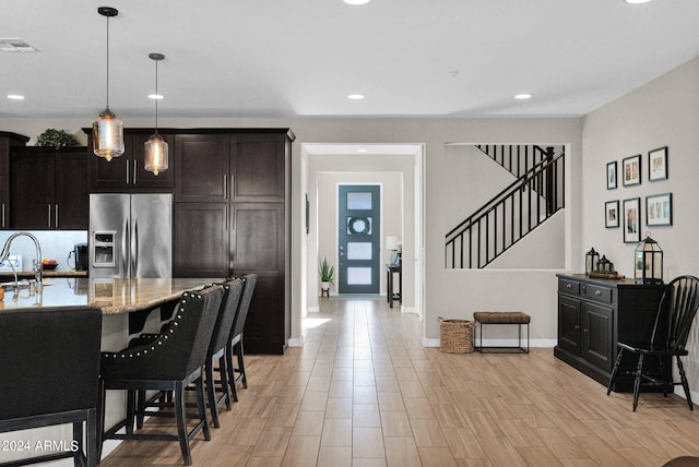 kitchen with light stone countertops, dark brown cabinetry, pendant lighting, light hardwood / wood-style flooring, and stainless steel refrigerator with ice dispenser