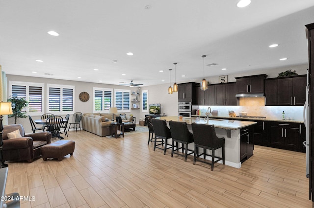 kitchen with a kitchen island with sink, ceiling fan, pendant lighting, light hardwood / wood-style flooring, and a breakfast bar