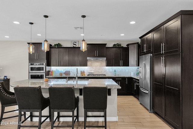 kitchen with a kitchen island with sink, pendant lighting, dark brown cabinetry, light hardwood / wood-style flooring, and stainless steel appliances