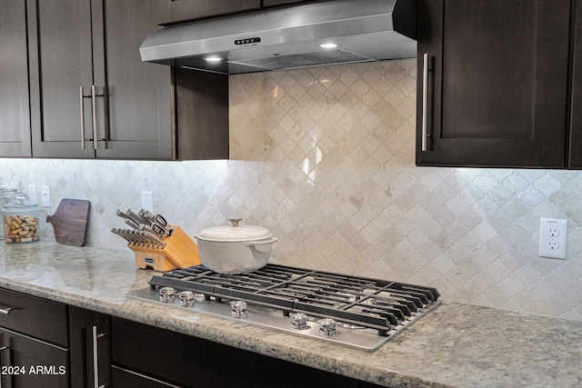 kitchen featuring light stone counters, dark brown cabinetry, tasteful backsplash, stainless steel gas cooktop, and exhaust hood