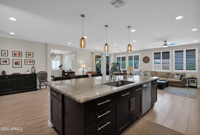 kitchen with light stone counters, ceiling fan, sink, pendant lighting, and a center island with sink