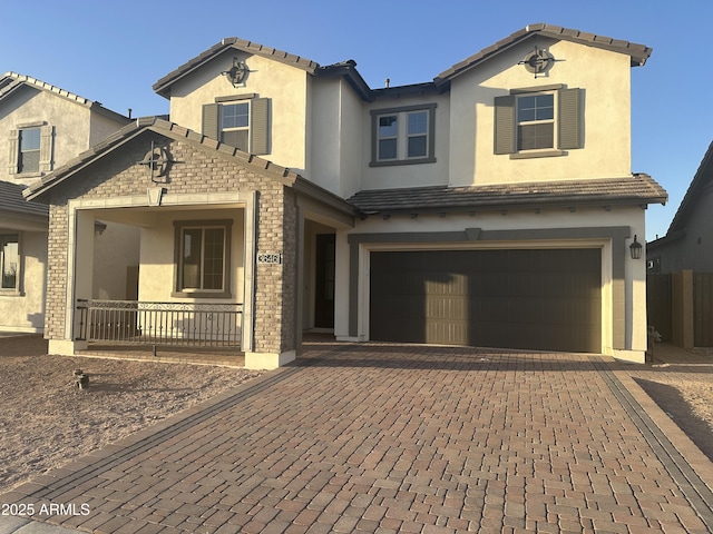 view of front of property with brick siding, a porch, stucco siding, decorative driveway, and a garage