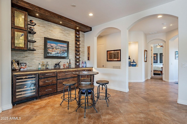 bar with dark brown cabinets, wine cooler, and backsplash