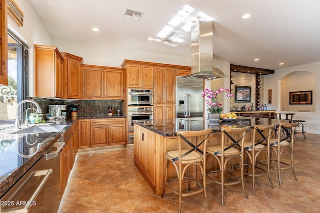 kitchen featuring sink, dark stone countertops, a kitchen breakfast bar, a center island, and island range hood