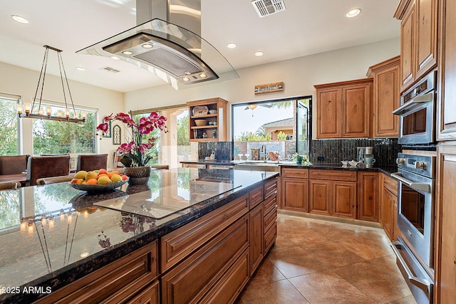 kitchen featuring pendant lighting, decorative backsplash, dark stone counters, island exhaust hood, and black electric cooktop