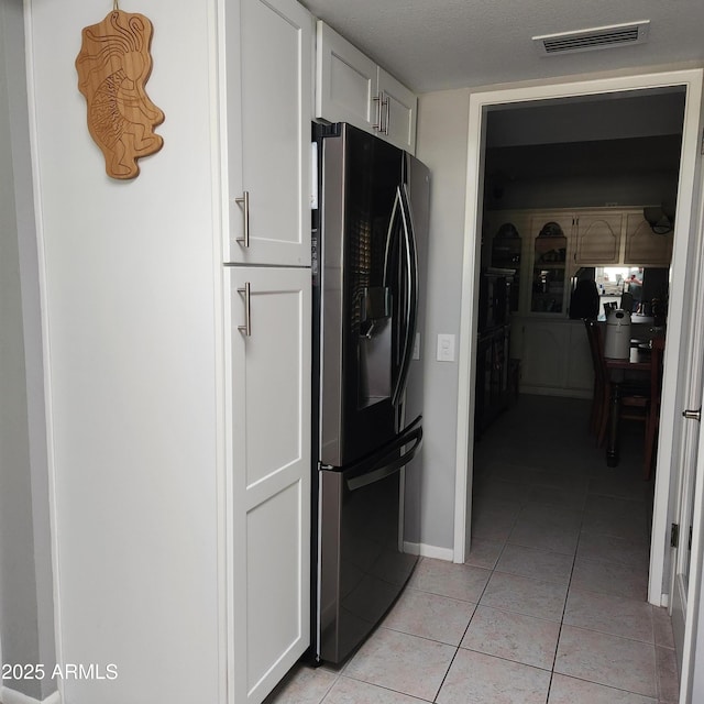 interior space with white cabinets, light tile patterned floors, and stainless steel fridge