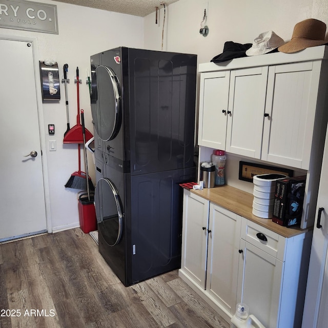 clothes washing area featuring cabinets, stacked washer / drying machine, a textured ceiling, and dark hardwood / wood-style flooring