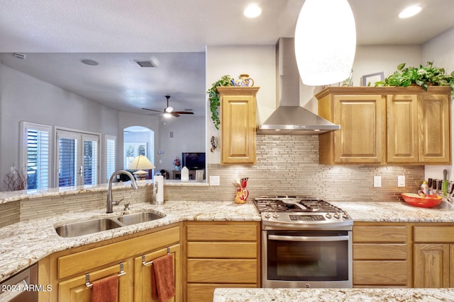 kitchen with ceiling fan, sink, wall chimney range hood, decorative backsplash, and appliances with stainless steel finishes