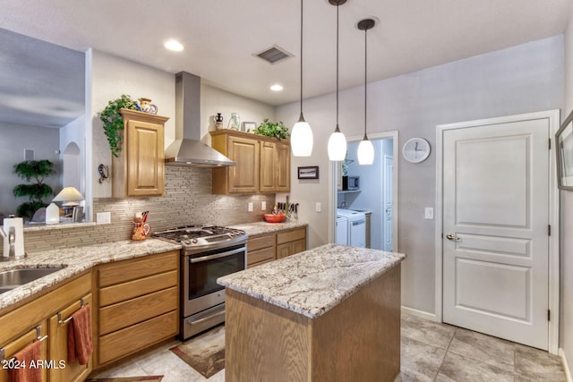 kitchen featuring decorative backsplash, stainless steel gas range oven, wall chimney exhaust hood, washing machine and clothes dryer, and a kitchen island