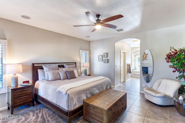 tiled bedroom with connected bathroom, ceiling fan, and a textured ceiling