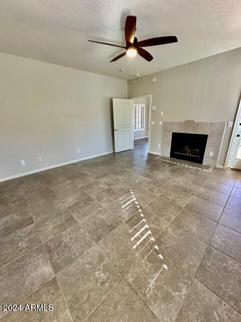 unfurnished living room featuring a tiled fireplace, ceiling fan, and a textured ceiling