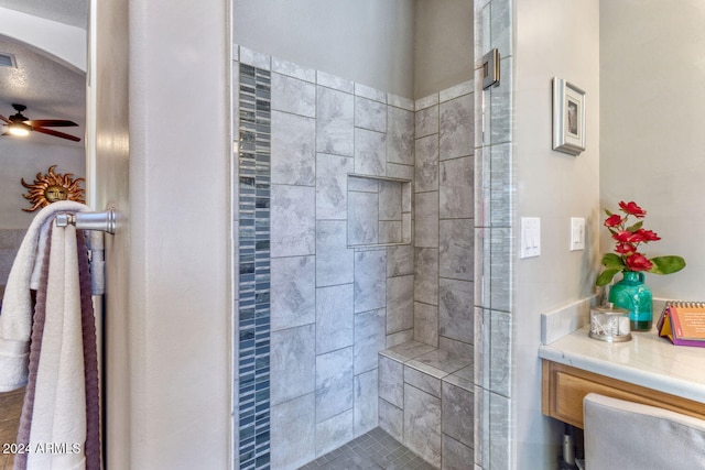 bathroom with a textured ceiling, ceiling fan, tiled shower, and tile patterned flooring