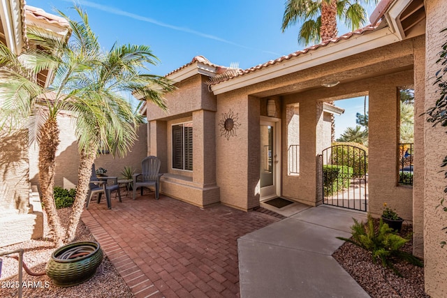 doorway to property featuring a gate, a patio area, a tiled roof, and stucco siding