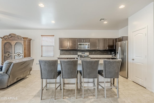 kitchen with dark brown cabinetry, a kitchen bar, visible vents, and stainless steel appliances