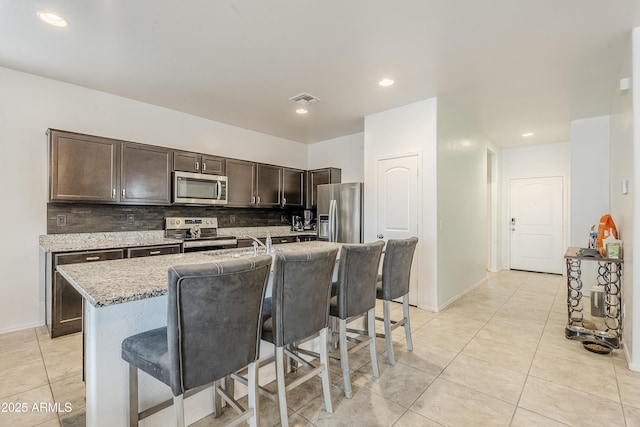 kitchen featuring dark brown cabinetry, visible vents, stainless steel appliances, a kitchen bar, and backsplash