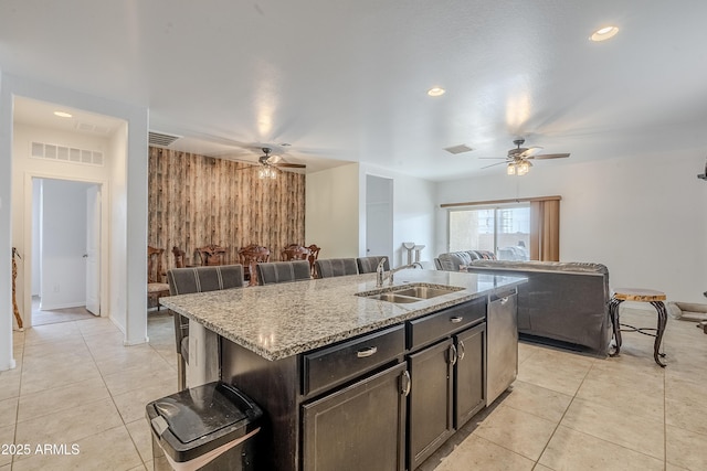 kitchen with visible vents, open floor plan, a sink, wood walls, and light stone countertops