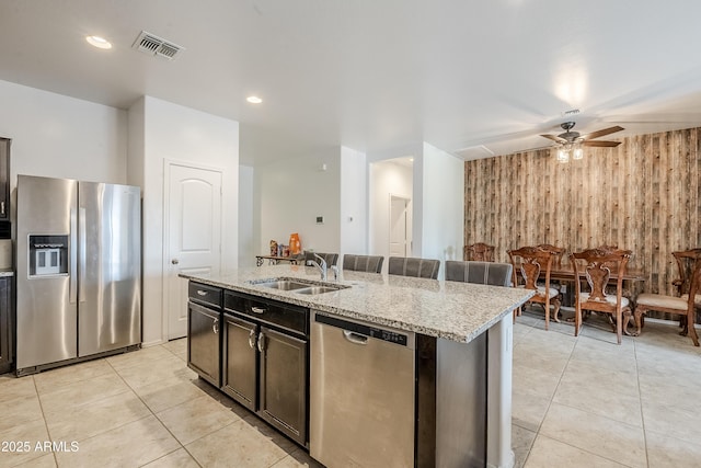 kitchen with light tile patterned floors, visible vents, appliances with stainless steel finishes, wood walls, and a sink