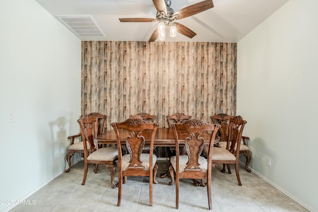 dining room with visible vents, ceiling fan, wooden walls, and baseboards