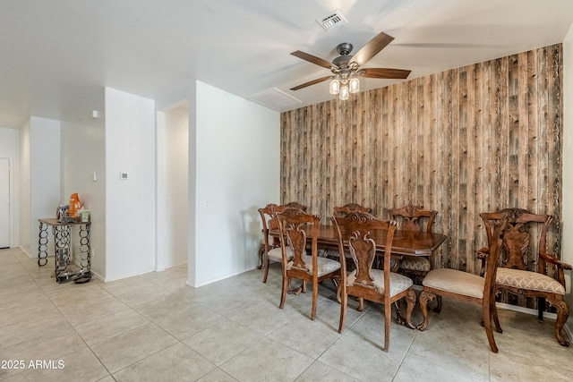 dining room featuring light tile patterned floors, ceiling fan, wooden walls, and visible vents