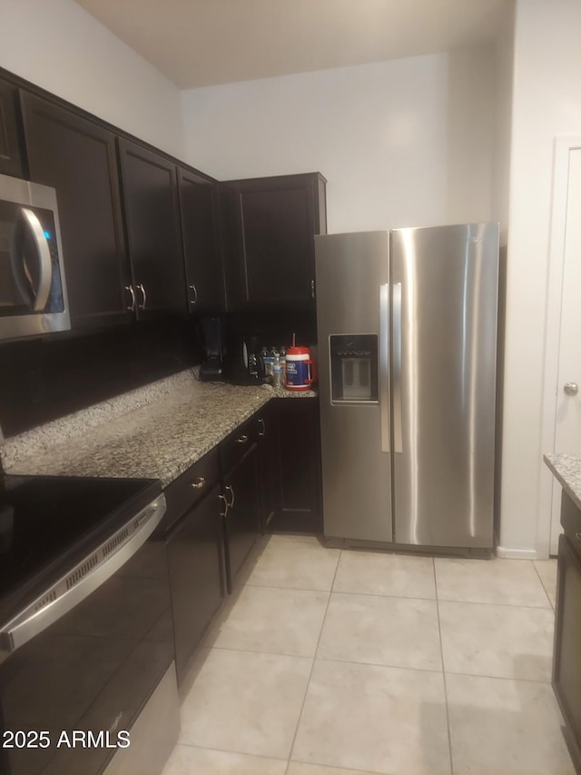 kitchen with appliances with stainless steel finishes, dark brown cabinets, light stone counters, and light tile patterned floors