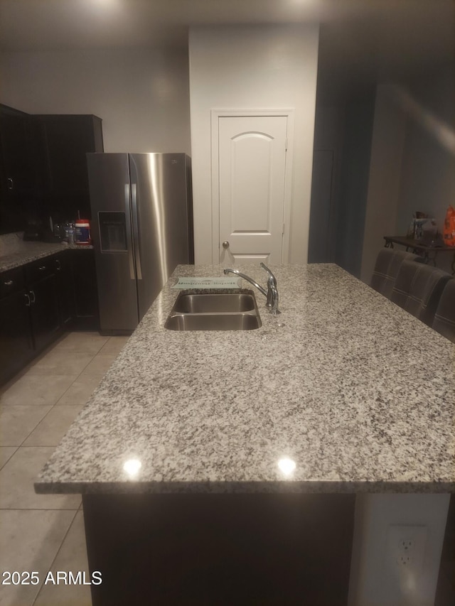 kitchen with light stone countertops, a kitchen island with sink, a sink, and stainless steel fridge with ice dispenser