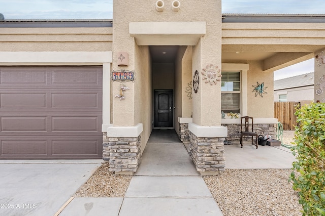 entrance to property featuring a garage, stone siding, fence, and stucco siding