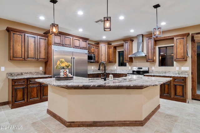 kitchen with an island with sink, decorative light fixtures, wall chimney range hood, and appliances with stainless steel finishes