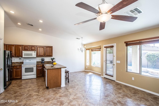 kitchen with a kitchen breakfast bar, dark stone counters, white appliances, decorative light fixtures, and lofted ceiling