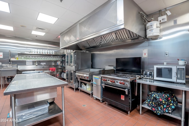 kitchen featuring stainless steel counters, wall chimney exhaust hood, high end black range oven, tile patterned flooring, and a paneled ceiling