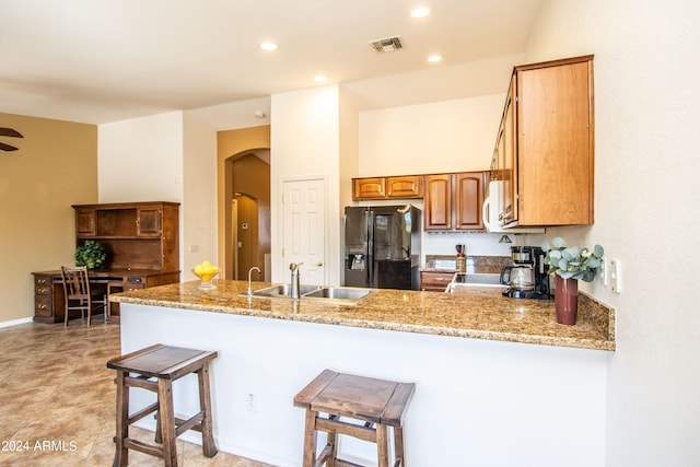 kitchen with black appliances, light stone counters, kitchen peninsula, and sink