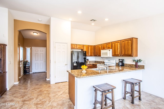 kitchen featuring white appliances, a high ceiling, a kitchen breakfast bar, light stone countertops, and kitchen peninsula