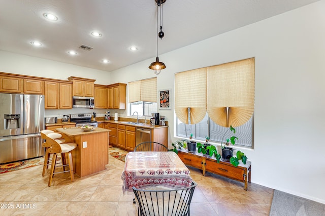 kitchen featuring sink, decorative light fixtures, appliances with stainless steel finishes, a kitchen breakfast bar, and a kitchen island