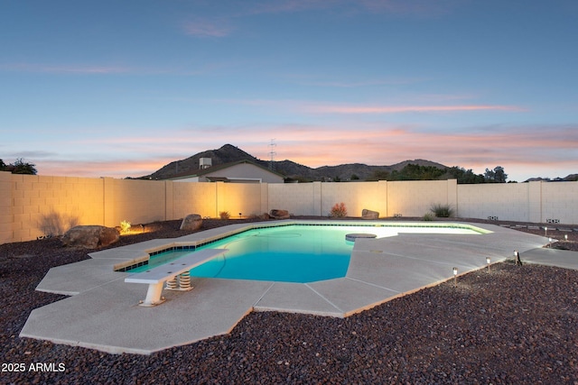 pool at dusk featuring a fenced in pool, a fenced backyard, a patio area, a mountain view, and a diving board