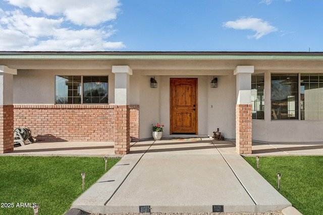 view of exterior entry featuring a porch, brick siding, and stucco siding