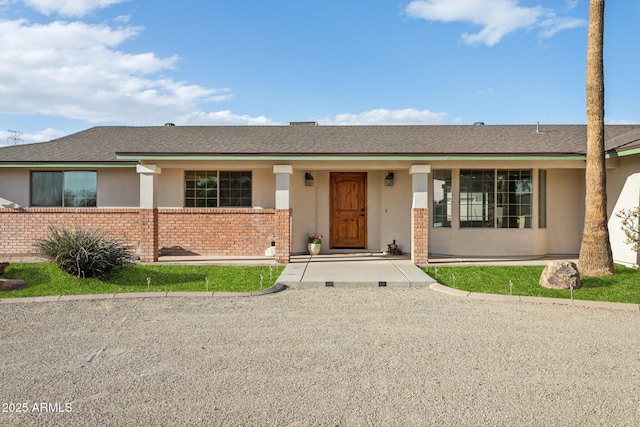 ranch-style house with brick siding, roof with shingles, and stucco siding