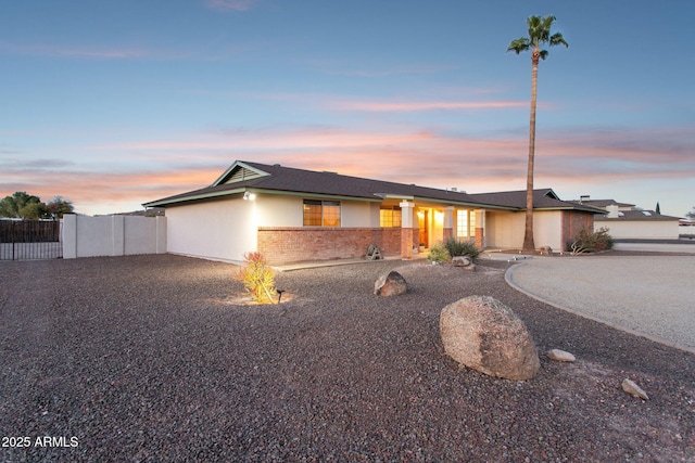 view of front of house with brick siding, curved driveway, fence, and stucco siding