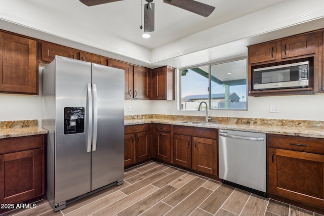 kitchen with wood finish floors, stainless steel appliances, a ceiling fan, a sink, and light stone countertops