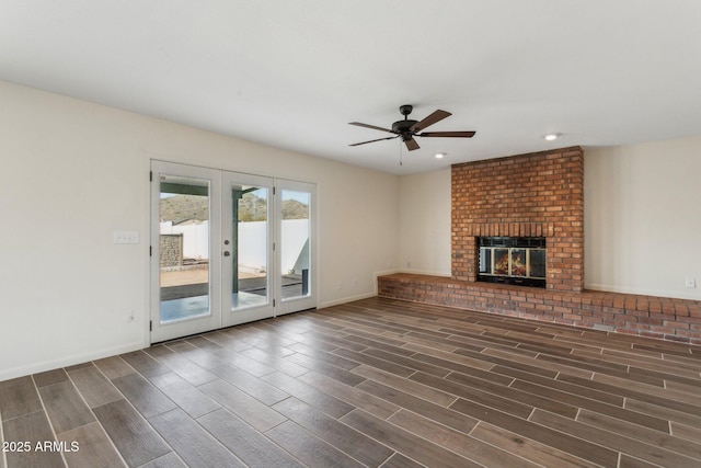 unfurnished living room with baseboards, a ceiling fan, french doors, a brick fireplace, and wood finish floors