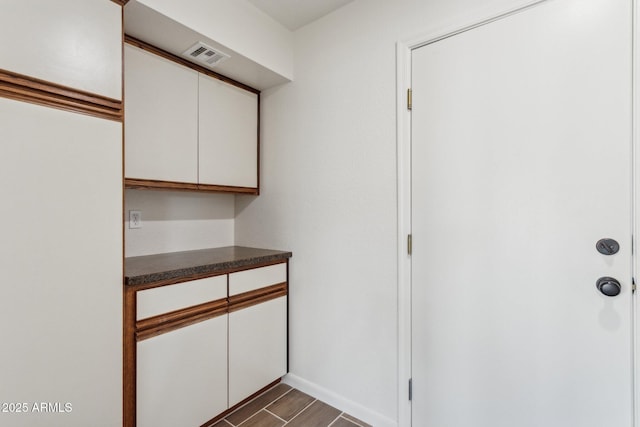 kitchen with dark countertops, visible vents, wood tiled floor, and white cabinetry