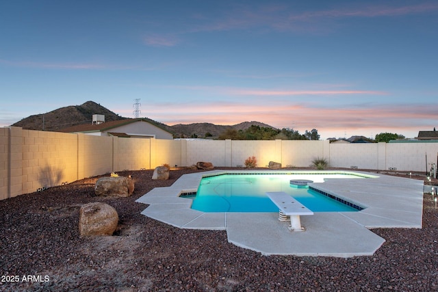 pool at dusk with a fenced backyard, a diving board, and a fenced in pool