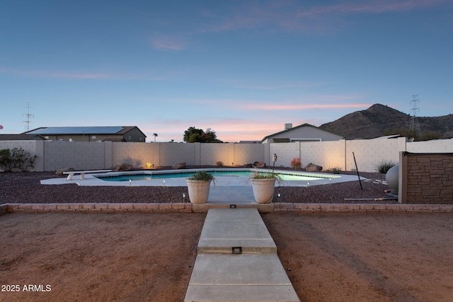 pool at dusk featuring a fenced in pool, a patio area, a fenced backyard, and a diving board