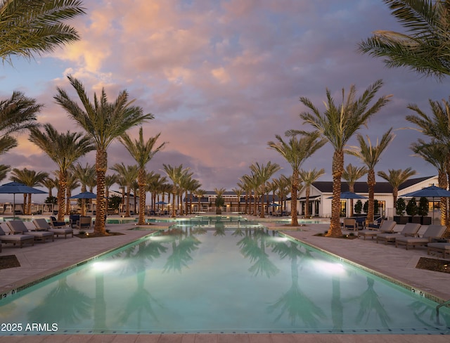 pool at dusk featuring a patio area and a community pool