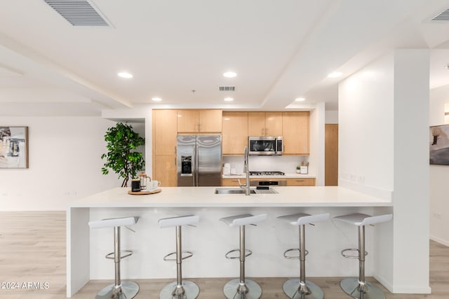 kitchen with appliances with stainless steel finishes, a kitchen bar, light wood-type flooring, and light brown cabinets