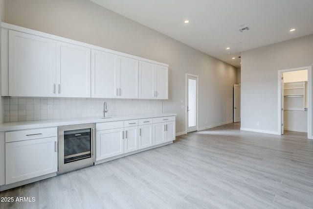 kitchen with sink, white cabinets, beverage cooler, decorative backsplash, and light hardwood / wood-style flooring